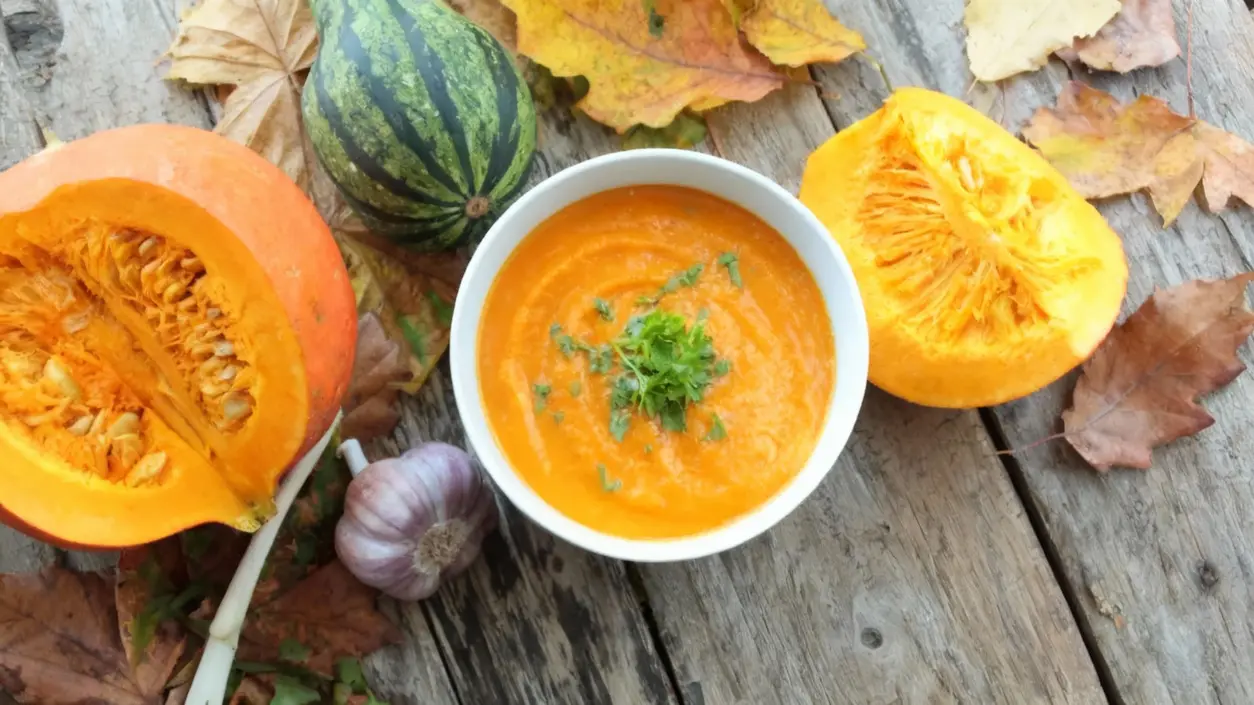 Zuppa di zucca in ciotola bianca con zucche fresche su tavolo di legno
