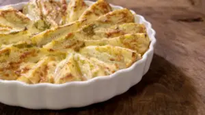 Finocchi al forno gratinati in una pirofila bianca su un tavolo di legno
