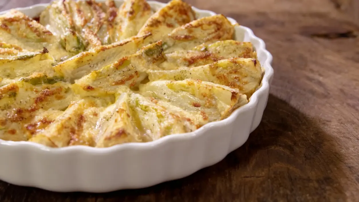 Finocchi al forno gratinati in una pirofila bianca su un tavolo di legno