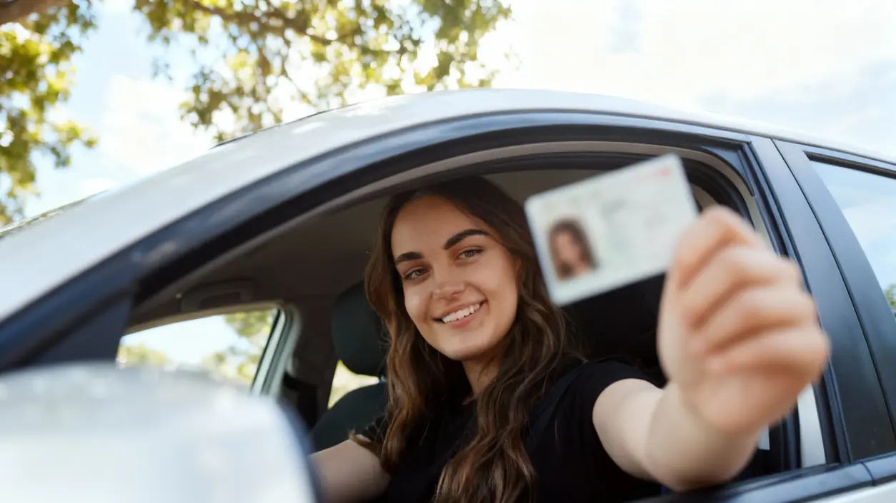 Persona al volante mostra una patente di guida attraverso il finestrino dell'auto