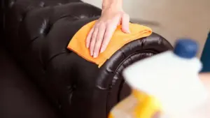 Mano che pulisce il bracciolo di un divano in pelle con un panno arancione
