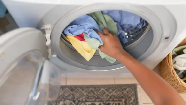 Una mano che inserisce asciugamani colorati in una lavatrice frontale aperta