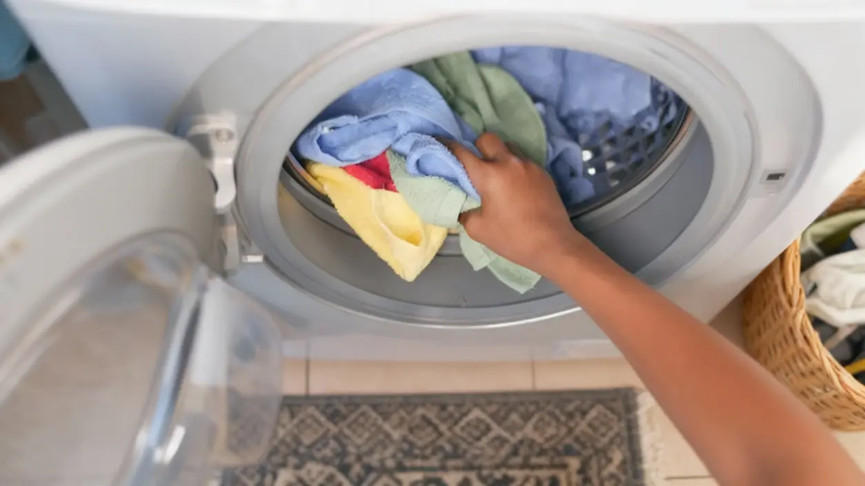 Una mano che inserisce asciugamani colorati in una lavatrice frontale aperta